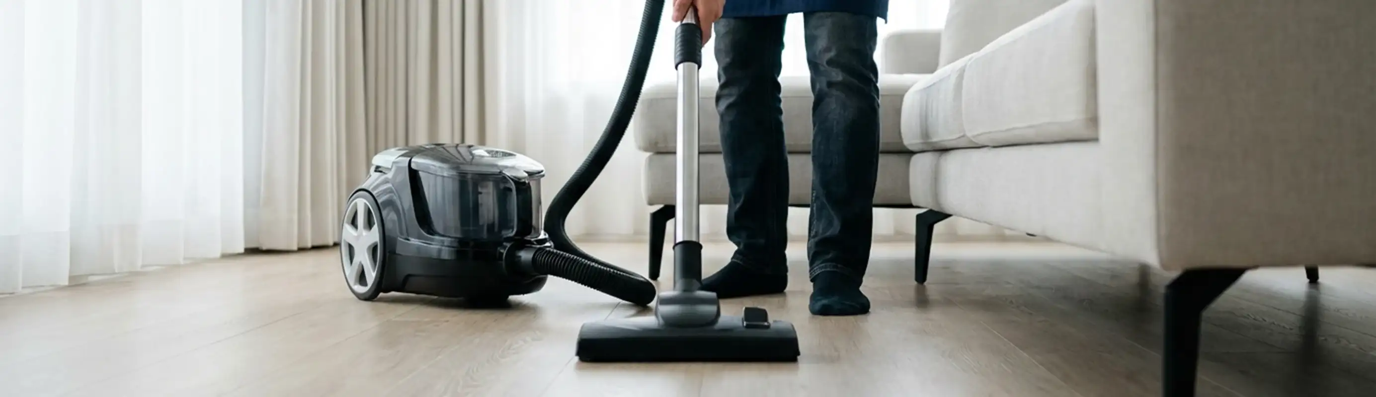 Professional house cleaner vacuuming a living room floor with a canister vacuum cleaner, Nashville, TN.