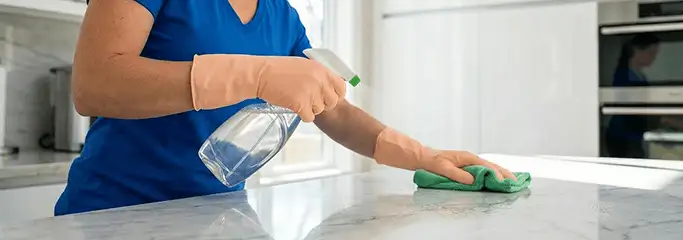 Maid service worker spraying and wiping a kitchen countertop with a microfiber cloth for sanitizing, Nashville, TN.
