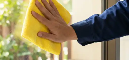 House cleaner wiping a glass window with a yellow microfiber cloth for streak-free cleaning, Nashville, TN.